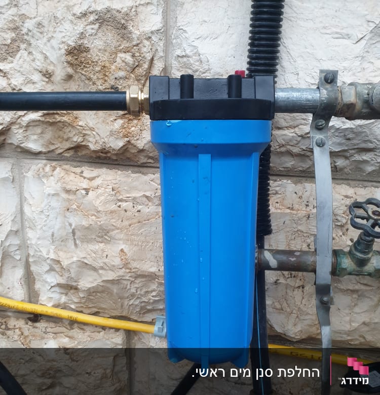 מסנן מים כחול מחובר לצינורות מתכת על קיר אבן